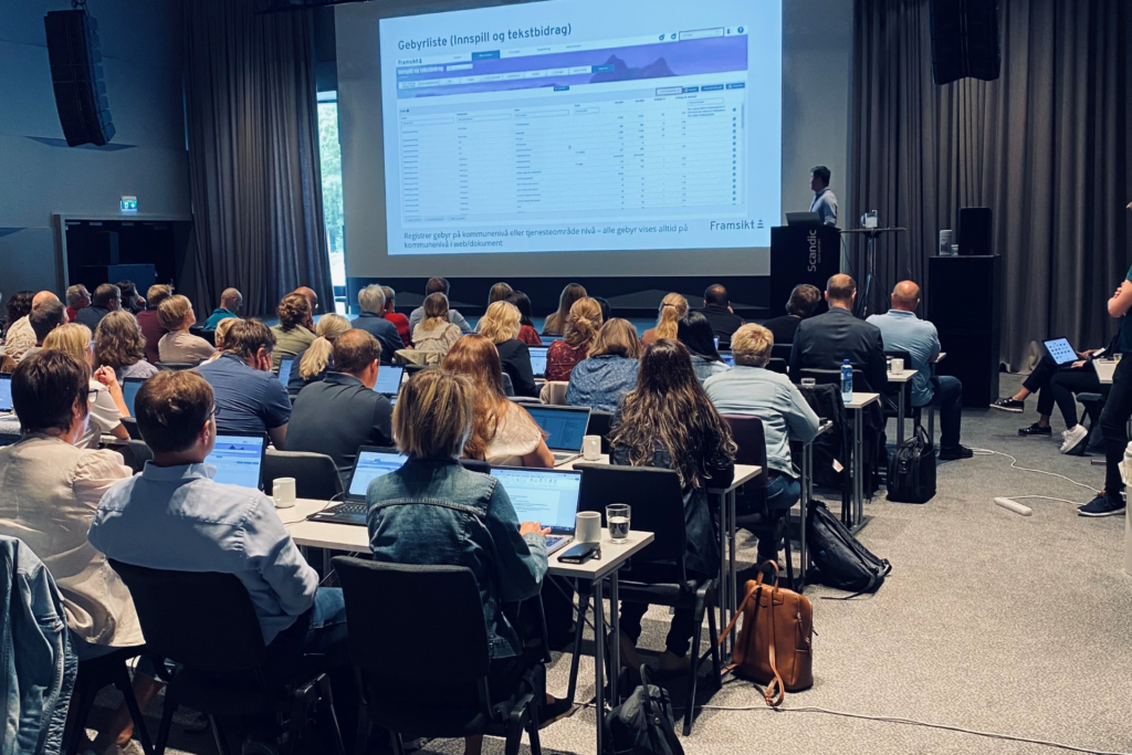 Bildet viser en en gruppe mennesker som sitter og ser på et foredrag